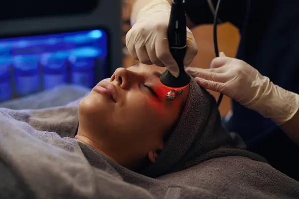 stock image Woman getting red light therapy and face massage in beauty salon