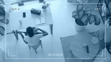 Güvenlik kamerası, erkek arkadaşı oturma odasında tablet bilgisayarda çalışırken siyah kadının gitar çalışını yüksek açılı görüyor.