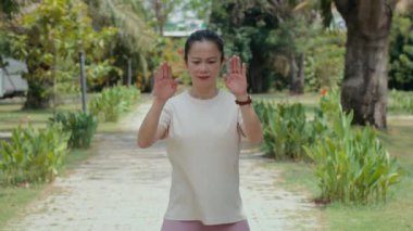 Orta yaşlı, aktif giyimli Asyalı bir kadının şehir parkında kol dairesi hareketlerini çekerken orta boy fotokopi.