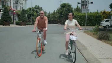 Çift ırklı orta yaşlı eşlerin haftasonunu dışarıda geçirirken bisiklet sürerken ve konuşurken çekilmiş görüntüleri.