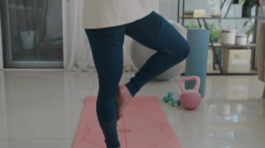 Yetişkin Asyalı bir kadının yoga yaparken, evde tek ayak üstünde meditasyon yaparken çekimini kaldır.