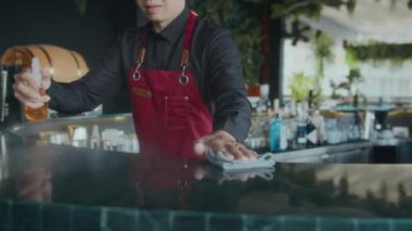 Lokantada çalışırken erkek garsonun tezgahın yüzeyini dezenfekte etmesi.