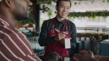 Garsonla konuşurken, içki ve yemek ısmarlarken, barın yanında oturan erkek misafirin omuzlarının üstünden.