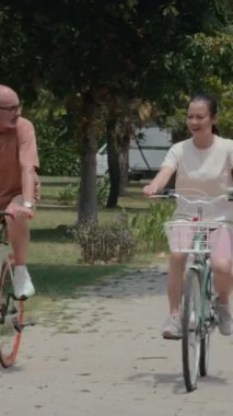 Parkta birlikte antrenman yaparken bisiklete binen çeşitli olgun erkek ve kadınların dikey çekimi.