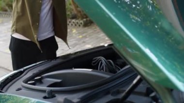 Erkek sürücünün arabanın bagajını açıp elektrik yüklemek için kabloyu kestiği sahne.
