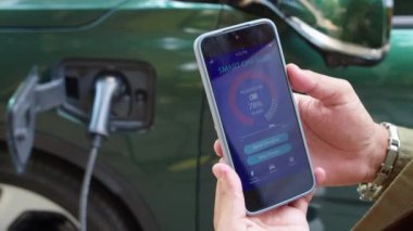 Şarj istasyonundaki elektrikli arabanın şarj durumunu izlerken akıllı telefondaki uygulamayı kullanan tanınmayan sürücünün ellerini kapat