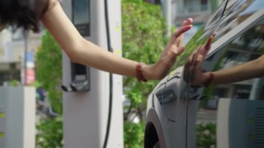 Şehirdeki şarj istasyonunda elektrik kablosu takan tanınmayan bir kadının görüntüsü.