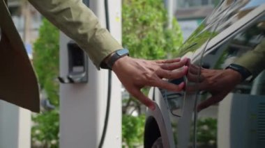 Şehir istasyonunda şarj kablosu takmak için elektrikli aracının kapağını açan tanınmayan bir adamın el kesimi.