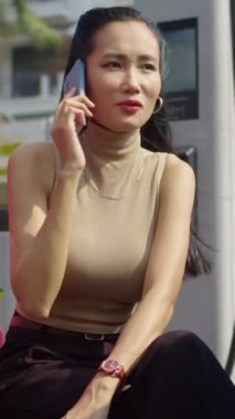 Asyalı genç iş kadınının şarj istasyonunda cep telefonuyla konuştuğu dikey çekim.