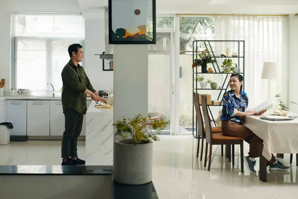 stock image Man standing in the kitchen and cooking dinner while his wife working at table