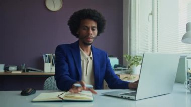 Kablosuz bilgisayar üzerinde çalışırken ve ofiste notlar alırken masasında kıvırcık saçlı dalgın siyah iş adamının orta boy fotoğrafı.