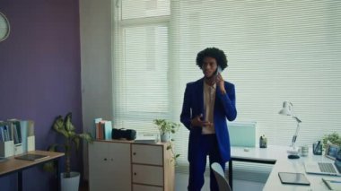 Orta ölçekli Afrikalı Amerikalı erkek proje yöneticisi iş ortağıyla ofisteki cep telefonunda fikirleri tartışıyor.