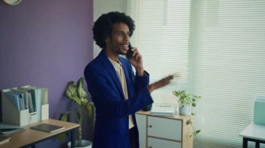 Ofiste çalışırken cep telefonunda resmi kıyafet danışmanlığı yapan siyah bir erkeğin görüntüsü.