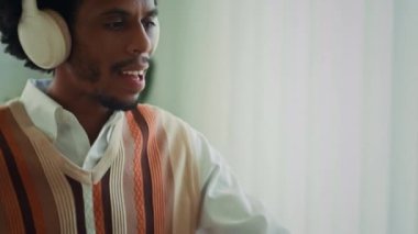 Afro-Amerikan kökenli bir adamın kulaklıkla müzik dinlerken, ofis masasında çalışırken görüntüsünü kaldır.