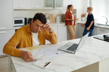 Adam faturaları sayıyor ve ailesi arka plandayken ödüyor.