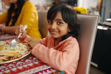 Ailesiyle yemek yerken kameraya gülümseyen Hintli çocuğun portresi.