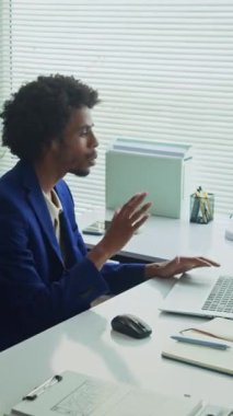 Ofisteki dizüstü bilgisayarın önünde otururken Afrikalı Amerikalı danışmanın müşteriyi ararken dikey görüntüsü.