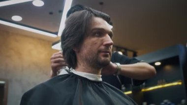 Genç kuaförün yeni saç kesimi için yetişkin erkek müşterinin saçlarını spreylediği düşük açılı bir manzara.