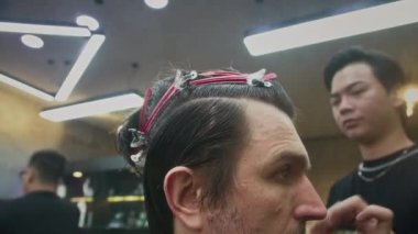 Erkek Asyalı uzmanların, kuaförde saç kesimi yaparken erkek müşterilerinin saçlarını spreyle nemlendirirken elde çekilmiş bir fotoğrafı.