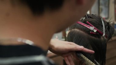 Erkek müşteri için berber dükkanında tarak ve makas kullanarak saç kesimi yapan stilistin omuzlarının üstünden.