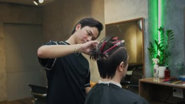 Berber dükkanındaki genç kuaföre saçını kestirirken, erkek müşterinin aynanın karşısında oturduğu orta boy bir fotoğraf.