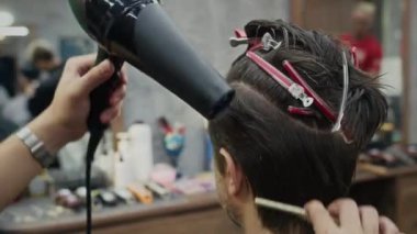 Berber dükkanında aynanın önünde oturan erkek müşterinin saçını şekillendirirken saç kurutma makinesi kullanan bir kuaför resmi.