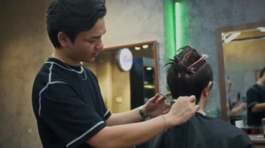 Genç Asyalı berber, berber dükkanında erkek müşteriye makas yapıyor.