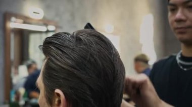 Berber dükkanında saç fırçalarken saç fırçalamak için tarağı kullanan Asyalı genç berber.