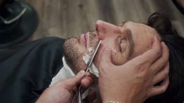 Orta yaşlı, beyaz bir adamın berber dükkanını ziyaret ederken yanaklarını, çenesini ve bıyıklarını traş etmesi.