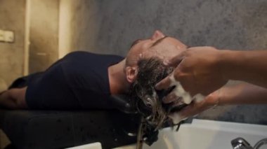 Erkek esmer, koltukta dinlenirken saçlarını yıkama modaya uygun bir salonda şampuanla temizliyor.