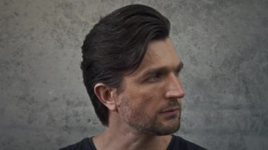 Gri arka planda kameraya bakan, şık saçlı, kendine güvenen beyaz bir adamın yakın portresi.