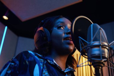 African American young singer singing in microphone and rehearsing her song in studio clipart