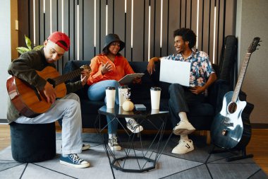 Müzik grubu kanepede oturup odada yeni şarkıları tartışıyor.