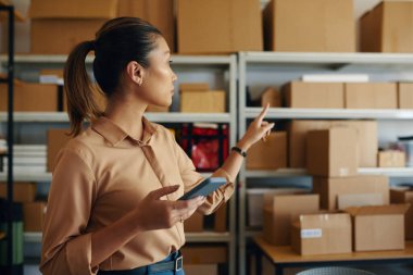 Depodaki sevkiyatı kontrol ederken akıllı telefonunu kullanan lojistik işçisi.