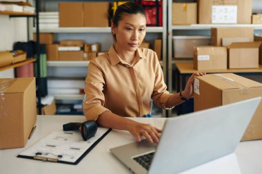 Asyalı genç bir kadın teslimattan önce paketin bilgilerini bilgisayara giriyor.