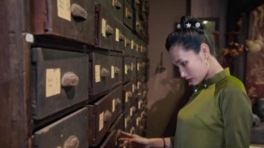 Kadın doğabilimcinin eczanedeki dolaptan bitkisel malzemeleri çıkarırken çekilen fotoğrafları.