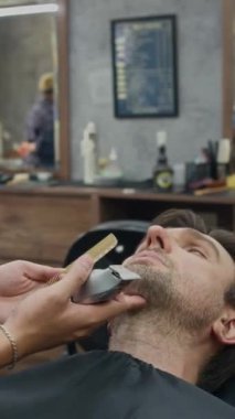 Kafkasyalı bir adamın son moda kuaförde sakalını keserken dikey pozu.