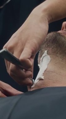 Bir adamın kuaförde keskin bir bıçakla boynu kesilirken dikey pozu.