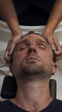Kafkasyalı bir adamın kuaförde saçını yıkadığı dik açılı görüntüsü.