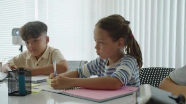 Sınav sırasında masada ders çalışan iki etnik ilkokul öğrencisinin el kamerası görüntüsü.