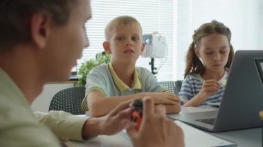 Mühendislik dersi sırasında çocuklarla konuşurken erkek öğretmenin robot modelini tutarken elde çekilmiş bir fotoğrafı.