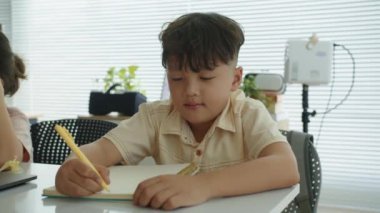 Sınıfta otururken kameraya gülümseyen küçük Asyalı bir çocuğun orta boy portresi.
