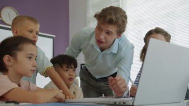 Bilgisayar dersinde dizüstü bilgisayarın önünde otururken genç erkek hoca ve çeşitli çocukların grup çalışması çekimleri.