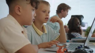 Modern okuldaki bilişim dersinde programlama kodları yazmayı öğrenen iki çocuğun el kamerası görüntüsü.