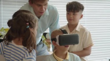 Erkek öğrencinin okuldaki öğretmeniyle grup kursunda arttırılmış gerçeklik kulaklığıyla uygulamayı test ederken orta boy fotoğrafı.