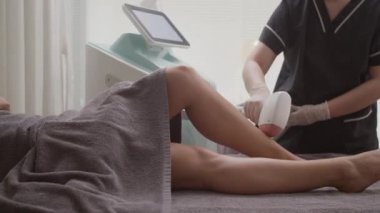 Tanımlanamayan güzellik uzmanının stüdyodaki saç çıkarma işlemi sırasında müşterinin bacaklarına IPV epilator sürerken görüntüsü.