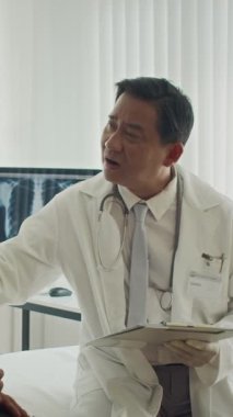 Asyalı pratisyen hekimin klinikteki konsültasyon sırasında hastayı neşelendirirken dikey çekimi.