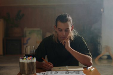 Genç tasarımcı iş yerinde otururken albüm çiziyor