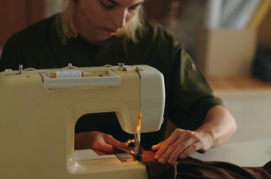 Genç moda tasarımcısı dikiş makinesiyle çalışıyor ve manken için yeni elbiseler dikiyor.