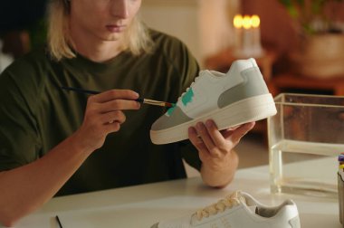 Moda tasarımcısı masada oturuyor ve müşteriler için spor ayakkabı boyuyor.